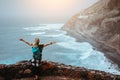 Tourist girl is happy to be on the end of long trekking route leading along cliff coastline with ocean waves from Royalty Free Stock Photo