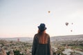 A tourist girl in a hat admires hot air balloons flying in the sky over Cappadocia in Turkey. Impressive sight. Royalty Free Stock Photo