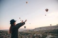 A tourist girl in a hat admires hot air balloons flying in the sky over Cappadocia in Turkey. Impressive sight. Royalty Free Stock Photo