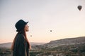 A tourist girl in a hat admires hot air balloons flying in the sky over Cappadocia in Turkey. Impressive sight. Royalty Free Stock Photo