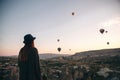 A tourist girl in a hat admires hot air balloons flying in the sky over Cappadocia in Turkey. Impressive sight. Royalty Free Stock Photo