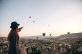 A tourist girl in a hat admires hot air balloons flying in the sky over Cappadocia in Turkey. Impressive sight. Royalty Free Stock Photo