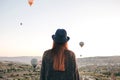 A tourist girl in a hat admires hot air balloons flying in the sky over Cappadocia in Turkey. Impressive sight. Royalty Free Stock Photo