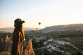 A tourist girl in a hat admires hot air balloons flying in the sky over Cappadocia in Turkey. Impressive sight. Royalty Free Stock Photo