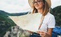 Tourist girl in hat holding in hands map and plans route leisure in nature during summer vacation on background green mountains Royalty Free Stock Photo