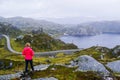 Tourist girl looks at the lake and the narrow road in the mountains at foggy cloudy weather in summer