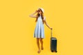 Tourist girl in a summer hat standing with a suitcase isolated on a blue background. Travel, summer vacation concept Royalty Free Stock Photo