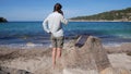 A tourist girl is talking on a smartphone on the seashore. The phone is charged by a solar panel that lies on a stone Royalty Free Stock Photo