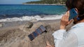 A tourist girl is talking on a smartphone on the seashore. The phone is charged by a solar panel that lies on a stone. Royalty Free Stock Photo