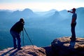 Tourist guide and photo enthusiast stay with tripod on cliff and thinking. Dreamy fogy landscape, blue misty sunrise in a beautifu Royalty Free Stock Photo