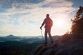 Tourist guide with pole in hand. Hiker with sporty backpack stand on rocky view point above misty valley. Sunny spring daybreak Royalty Free Stock Photo