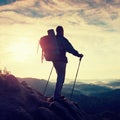 Tourist guide with pole in hand. Hiker with sporty backpack stand on rocky view point above misty valley. Sunny spring daybreak Royalty Free Stock Photo