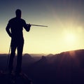 Tourist guide show the right way with pole in hand. Hiker with sporty backpack stand on rocky view point above misty valley. Sunny Royalty Free Stock Photo