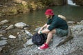 Tourist guy with backpack sitting near lake in a wild summer wood. Expedition