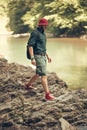 Tourist guy with backpack sitting near lake in a wild summer wood. Expedition