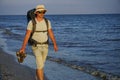 A tourist guy with a large backpack, dressed in shorts, a Panama T-shirt and glasses, walks along the wet sand along the sea coast Royalty Free Stock Photo