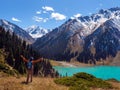 A tourist guy in an orange jacket and hat is hiking high in the mountains overlooking a beautiful turquoise lake