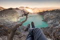 Tourist hanging legs on crater Kawah Ijen with emerald lake at s