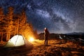 Tourist have a rest in his camp near the forest at night, pointing at beautiful night sky full of stars and milky way Royalty Free Stock Photo