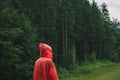 Tourist hiker in red raincoat stands in rain in mountains against coniferous forest background and looks away. Minimalistic photo Royalty Free Stock Photo