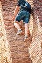 Tourist in jeans shorts and teeshirt with small backpack climbs steep narrow steps in ancient ruin - cropped