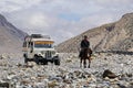 A tourist jeep and a local resident riding a horse among the Himalayan mountains on the way to Upper Mustang