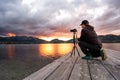 A tourist keen on photography bends down to adjust his camera to get a good picture of the spectacular cloudy sunset with the sun