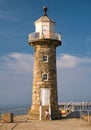 A tourist looks at a phone while sitting on stone steps at the foot of the historic sandstone Whitby West Pier Lighthouse Royalty Free Stock Photo