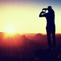 Tourist make frame with palms and fingers on both hands. Hiker on rocky cliff, daybreak in rocky mountains.