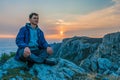 Tourist man in a blue jacket sits on a rock high in the mountains, above the clouds and enjoys the sunset Copy space. The concept Royalty Free Stock Photo