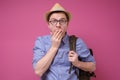 Tourist man in hat and backpack covering his mouth with his hands and looking to camera with fear Royalty Free Stock Photo