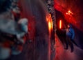 Tourist man holding red glow lamp in deep narrow glacial ice cave