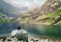 Tourist man sits next to a clear lake under wonderful mountains in the Tatras during tourist trip. Freedom, adventure concept.