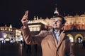 Tourist man taking selfie on smartphone at night on Market square in Krakow Poland. Travel around Europe
