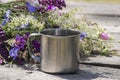 Tourist metal cup next to the flowers stands on a gray wooden table