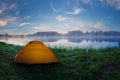 Tourist orange tent on green grass of foggy lake at sunrise Royalty Free Stock Photo