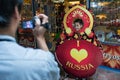 A tourist photographs a child, a Russian doll with the inscription I love heart Russia in the seaport on the background of a