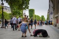 A tourist places coins in the cup of a woman begging on the sidewalk of Champs-Elysees