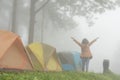 tourist raise hand with happiness near tent in mist & fog. camping in forest. people, travel, vacation concept Royalty Free Stock Photo