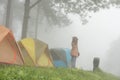 tourist raise hand with happiness near tent in mist & fog. camping in forest. people, travel, vacation concept Royalty Free Stock Photo