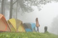 tourist raise hand with happiness near tent in mist & fog. camping in forest. people, travel, vacation concept Royalty Free Stock Photo