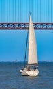 Tourist recreation sailboat sailing on the red steel 25 de Abril Suspension Bridge over the Tagus River in the city of Lisbon, Royalty Free Stock Photo