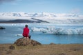 Tourist in a red jacket sits on the shores of the glacial lagoon Royalty Free Stock Photo