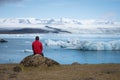 Tourist in a red jacket sits on the shores of the glacial lagoon Royalty Free Stock Photo