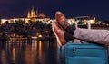 Tourist is relaxing near Prague Castle at night in Prague with legs on his luggage. Travel concept.