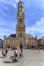 Tourist riding a bike in front of the Belfry Tower in the market square in the center of Bruges, a beautiful medieval town in Belg