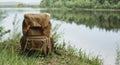 Tourist`s brown backpack on the shore of a river. A great trip to nature in a dense green forest with a reservoir