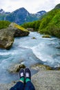 Tourist`s  legs above the river which is located near path to the Briksdalsbreen Briksdal glacier. Norway Royalty Free Stock Photo