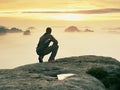 Tourist sit on peak of sandstone rock and watching into colorful mist and fog in morning valley. Sad man Royalty Free Stock Photo