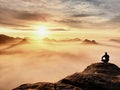 Tourist sit on peak of sandstone rock and watching into colorful mist and fog in morning valley. Sad man Royalty Free Stock Photo